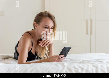 Junge kaukasier Frau mit ihrem Telefon auf dem Bett Stockfoto