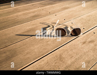 Klar Sonnenbrille warf einen langen Schatten auf einen hölzernen Tisch gerahmt Stockfoto