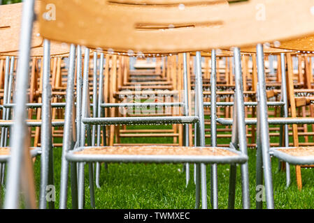 Stühle aus Holz close-up stand draußen im Park im Regen. Leere Auditorium, grünes Gras, Bäume und Stühlen mit Wassertropfen. Stockfoto