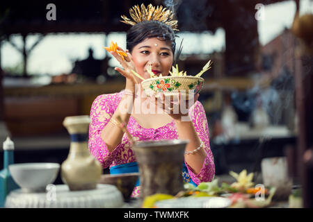 Lächelnd Balinesischen Frau im rosa Kleid und Blume Gaben an die Götter einen hinduistischen Tempel Stockfoto