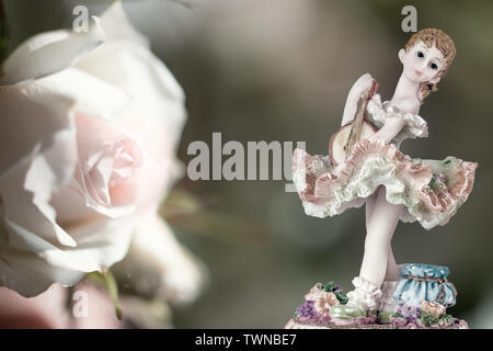 Jahrgang Mädchen Figur trägt Petticoat mit Gitarre und eine weiße Rose auf Cremigem grünen Hintergrund. Zusammensetzung Stockfoto