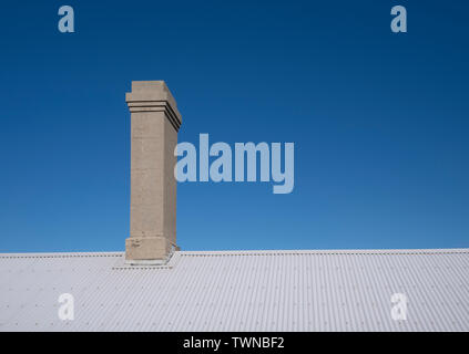 Alte Kamin auf Wellblech Dach vor einem klaren blauen Himmel Stockfoto