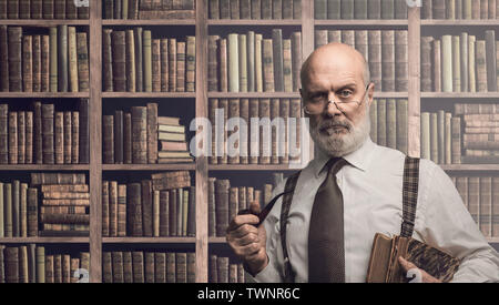Sicher leitenden akademischen Professor Rauchen einer Pfeife und in der Bibliothek Posing, alte Bücherregale im Hintergrund Stockfoto