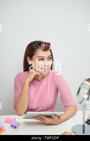 Nachdenklich hübsche Frau tragen Lockenstäbe mit Tablet PC im Wohnzimmer sitzen Stockfoto