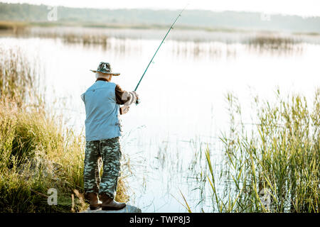 Älterer Mann angeln auf dem See am frühen Morgen, Rückansicht Stockfoto