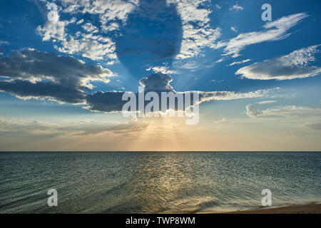 Eine Wolke wie ein U-Boot auf dem Meer, wegen dem die Strahlen der Sonne durch bei Sonnenuntergang brechen Stockfoto