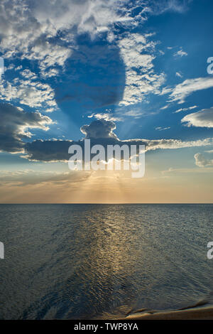Eine Wolke wie ein U-Boot auf dem Meer, wegen dem die Strahlen der Sonne durch bei Sonnenuntergang brechen Stockfoto