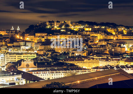 Lissabon bei Nacht. Die Hauptstadt von Portugal mit der Burg Sao Jorge vom Aussichtspunkt. Beleuchtete Skyline bei Nacht mit Gebäude und Dächer. Stockfoto