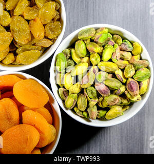 Gesunde Snacks in weißen Schalen auf einem Tisch, Pistazien, Rosinen und Weich getrocknete Aprikosen, mit keine Menschen. Stockfoto