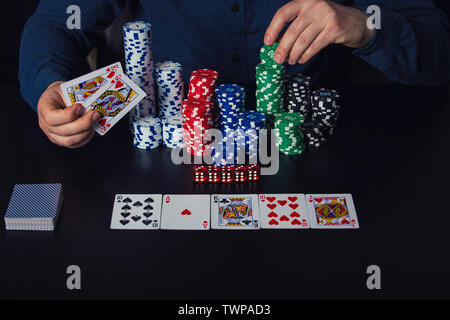 Die Hände schließen, bis der junge Mann poker Spieler mit Karten und Chips am Tisch. Spielen Turnier Sieger erfolg konzept auf dunklem Hintergrund. Stockfoto