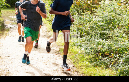 Eine Gruppe von Jungen High School Querfeldeinläufer zusammen Training auf einem unbefestigten Weg in den Wald. Stockfoto