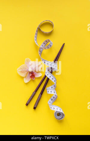 Asiatischen Ernährung Konzept. Stäbchen und Maßband auf gelbem Hintergrund, kopieren. Diät, asiatische gesunder Lebensstil, Gewichtsverlust Konzept. Stockfoto