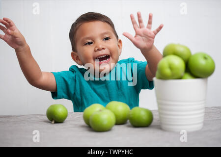 Ein Junge seine Freude für frisches Obst zum Ausdruck zu bringen, mit den Armen in der Luft und spielt mit einem Eimer mit grünen Äpfeln. Stockfoto