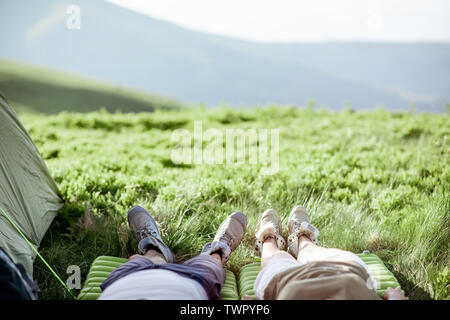 Paar liegen auf der grünen Wiese, während hohe unterwegs in den Bergen, in der Nähe der Beine in Trekking Schuhe Stockfoto