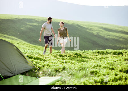 Junges Paar Wandern auf der grünen Wiese in der Nähe des Campingplatzes während der Fahrt hoch in den Bergen Stockfoto