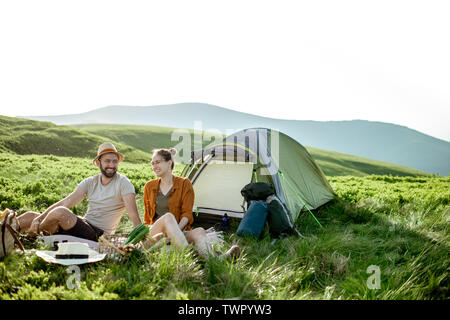 Junge und freundliche Paar bei einem Picknick auf dem Campingplatz während der Fahrt hoch in die Berge bei Sonnenuntergang Stockfoto