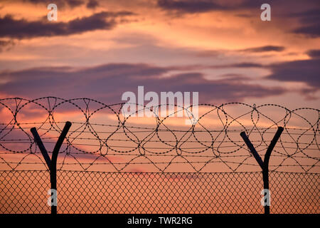 Abschnitt einer Kette Link Zaun mit Stacheldraht und vor einem Sonnenuntergang Stockfoto