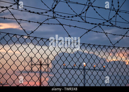 Details einer Kette Link Zaun mit Stacheldraht und vor einem Sonnenuntergang am Flughafen Stockfoto