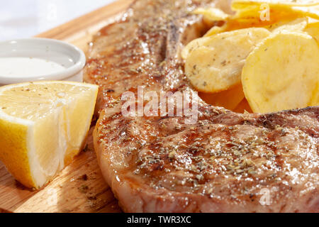 Große Rindersteak mit Oregano auf Holz- Oberfläche serviert mit Zitrone, weißen Sauce und Scheiben von Pommes frites Stockfoto