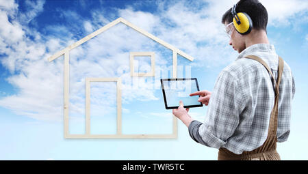 Hausbau renovierung Konzept Heimwerker Tischler mann Touchscreen der digitalen Tablet, isoliert mit dem Modell eines Holzhauses auf blauen Himmel bac Stockfoto