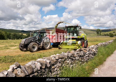 Die Landwirte profitieren Sie von einem Tag auf trockener Sommer Wetter Mähwiesen zu schneiden und das Gras sammeln für Silage, Austwick, North Yorkshire. Stockfoto