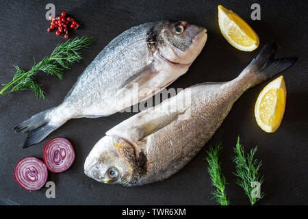 Frische rohe dorado Fisch mit Gemüse auf schwarzem Teller serviert. Stockfoto