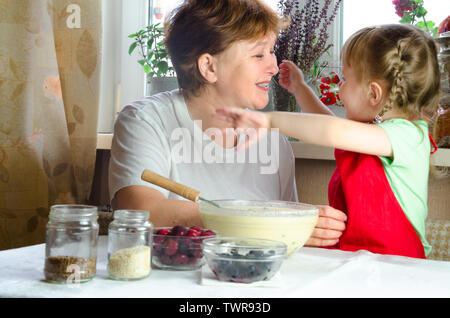 Portrait von Gesichtern, Händen glücklich Braunhaarige granny Hug Enkelin. Kleinkind Mädchen spielen mit Großmutter auf Küche. Kind Baby halten Oma und Lachen Stockfoto