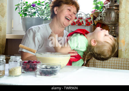 Portrait von Gesichtern, Händen glücklich Braunhaarige granny Hug Enkelin. Kleinkind Mädchen spielen mit Großmutter auf Küche. Kind Baby halten Oma und Lachen Stockfoto