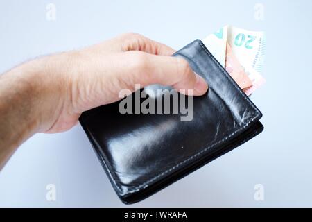 Die Hand eines Mannes hält, stiehlt, ein schwarzes Leder-Etui mit Geld aus der Bank, in Euro. Stockfoto