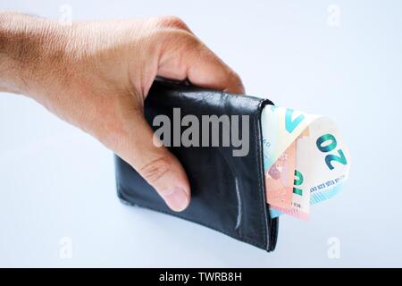 Die Hand eines Mannes hält, stiehlt, ein schwarzes Leder-Etui mit Geld aus der Bank, in Euro. Stockfoto
