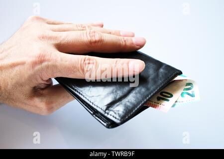 Die Hand eines Mannes hält, stiehlt, ein schwarzes Leder-Etui mit Geld aus der Bank, in Euro. Stockfoto
