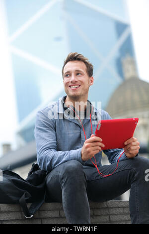 Urban Young Professional Mann mit Tablet Computer sitzt in Hongkong außen mit App auf 4g Wireless gerät Kopfhörer tragen. Casual Young Urban professional Mann in seinem späten 20s. Stockfoto