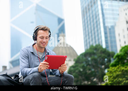 Mann auf tablet pc in video Gespräch in draußen sitzen mit App auf 4g Wireless gerät Kopfhörer tragen. Casual Young Urban professional Mann in seinem späten 20s. Hong Kong. Stockfoto