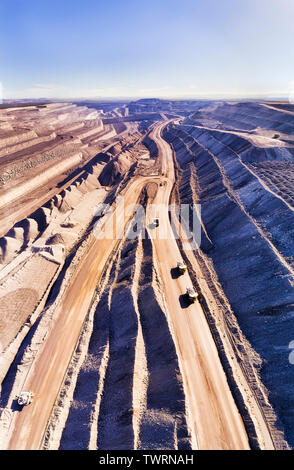 Tief aufgeschnitten Black Coal Mine von Thorley mount in Hunter Valley, Australien. Vertikal von Oben nach Unten Blick auf riesigen Trucks moving raw Mineralien. Stockfoto