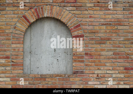 Attraktive alte Robuste beige Wand mit bunten Steinen in unterschiedlichen Schattierungen von rot gespickt, die eine an Bord bis Backstein Fenster Stockfoto