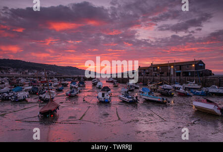 Lyme Regis, Dorset, Großbritannien. 23. Juni 2019. UK Wetter: der Himmel über dem historischen Cobb Hafen glüht mit leuchtend roten Sonnenaufgang Farben als Firey Wolken bringen einen Urlaub in der Sonne in Lyme Regis am Sonntag Morgen. Credit: Celia McMahon/Alamy Leben Nachrichten. Stockfoto