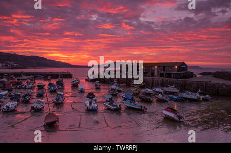 Lyme Regis, Dorset, Großbritannien. 23. Juni 2019. UK Wetter: der Himmel über dem historischen Cobb Hafen glüht mit leuchtend roten Sonnenaufgang Farben als Firey Wolken bringen einen Urlaub in der Sonne in Lyme Regis am Sonntag Morgen. Credit: Celia McMahon/Alamy Leben Nachrichten. Stockfoto