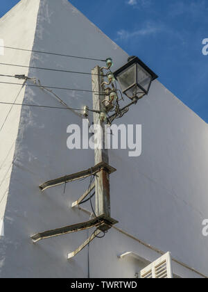 Straßenbeleuchtung, kombinierte Stromleitungen, Holzpfosten, weiß getünchte Wand, Niederspannung, Strom, Versorgung, spanische Elektrik, Heath Robinson, undurchführbar. Stockfoto