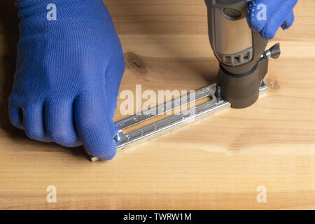 Ein Mann in Blau Handschuhe ist Schneiden ein Loch in einer Sperrholzplatte. Stockfoto