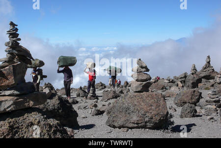 Mount Kilimanjaro/Tansania: 5. Januar 2016: Torhüter tragen Ausrüstung und Material durch eine Steinwüste mit vielen Steinhaufen auf dem Mount Kilimanjaro Stockfoto