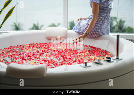 Junge Frau entspannend auf Luxus Badewanne mit Rosen Blätter in Wasser Stockfoto