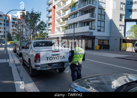 Ein Parkplatz Patrol Officer schreibt eine Verletzung Hinweis für einen illegal geparkten Fahrzeug in die Innenstadt von Sydney Vorort von Wolli Creek, Australien Stockfoto