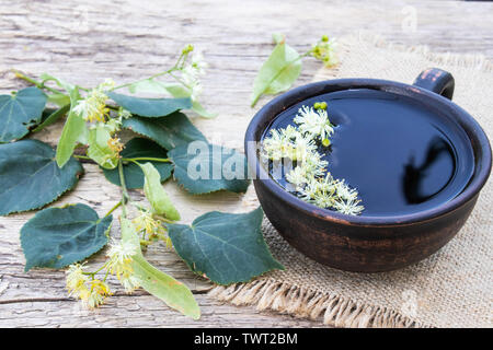 Eine Tasse Tee in der Nähe der Linden Kalk Blumen auf dem Hintergrund der alten Boards. linden Blumen und eine Tasse Kaffee. Kräutertee. Kälte und Grippe zu beheben. Stockfoto