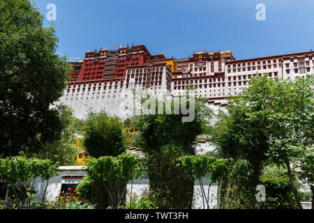 In der Nähe der Hauptgebäude der Potala Palast mit Bäumen und Sträuchern. Chinesische Fahne winken auf der Oberseite des Palastes. Unesco-Welterbe. Denkmal, Festung. Stockfoto
