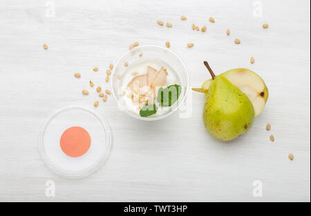 Joghurt birne Schichten und Minze und Pinienkernen liegen in einem Lunch Box auf einem weißen Tisch mit Pinienkernen und Birne Schichten, zerstreut werden. Gesunde Ernährung Konzept Stockfoto