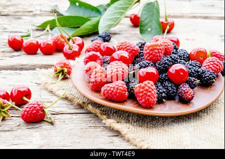 Saftige frische und köstliche Beeren, Kirschen, Himbeeren, Maulbeeren in einer Schüssel auf Holz- Hintergrund. Close-up Stockfoto