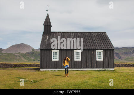 Person auf dem Hintergrund der berühmten Schwarzen Kirche von Budir auf Snaefellsnes Halbinsel Region in Island. Auf Island Willkommen. Wanderlust Konzept. Stockfoto