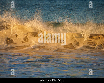 Die untergehende Sonne scheint ihr letztes Licht für den Tag auf glühenden Wellen, die in den Strand, Forster NSW Australia, eindringen Stockfoto