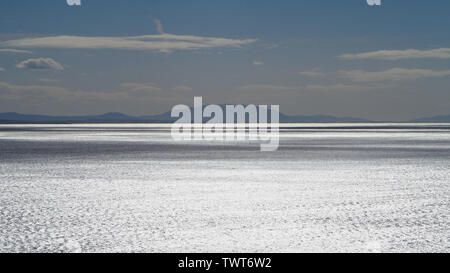 Pazifischer Ozean, Meerwasser, das im Sonnenlicht silbern schimmert, vor Hügeln im Hintergrund, blauer Himmel, Wolken, die surreal wirken, Forster NSW, Australien Stockfoto