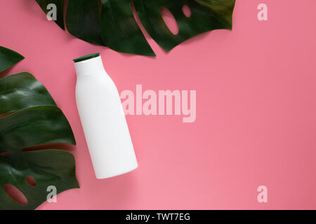 Kosmetik natur kosmetik Hautpflege Konzept. weiße Flasche Container mit leeres Etikett für das Branding mock up, dekorieren mit grünen tropischen Blättern auf Rosa b Stockfoto